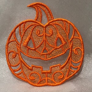 May include: Orange embroidered pumpkin with a carved jack-o'-lantern face. The pumpkin is made of a delicate lace-like material.
