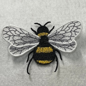May include: A black and yellow embroidered bumble bee with white wings. The bee is on a white background.
