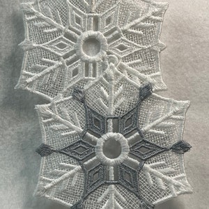 May include: Two white snowflake ornaments, one with a silver snowflake design in the center.