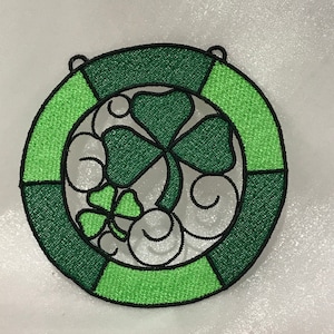 May include: A green and black embroidered shamrock wreath with a three-leaf clover design.