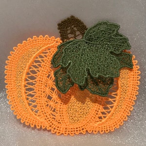 May include: Orange and green crocheted pumpkin with a leafy stem. The pumpkin is made of delicate lace and has a gradient of color from light orange to dark orange.
