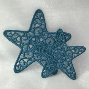 May include: Two teal blue lace star ornaments with intricate designs.