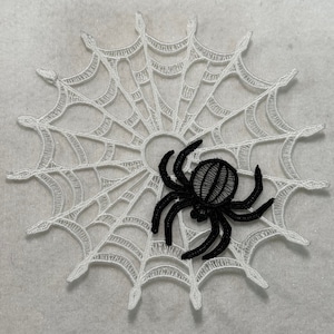 May include: A white lace spiderweb with a black spider in the center. The spiderweb is a decorative item for Halloween.