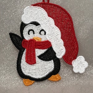 May include: A white penguin wearing a red Santa hat and a red scarf. The penguin is embroidered and has a cheerful expression.