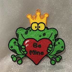 May include: Green frog wearing a yellow crown holding a red heart that says "Be Mine".