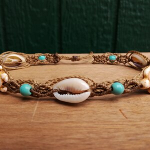 Peut inclure: Un bracelet en macramé marron avec des perles turquoise, une coquille de cauris et deux breloques en coquille de tortue blanche.