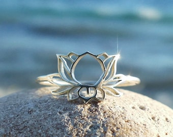 Puede incluir: Un anillo de plata con un delicado diseño de flor de loto. El anillo está sobre una piedra de color gris claro.
