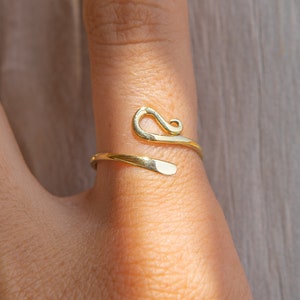 Puede incluir: Un anillo ajustable de metal dorado con un diseño abstracto único. El anillo es liso y pulido.