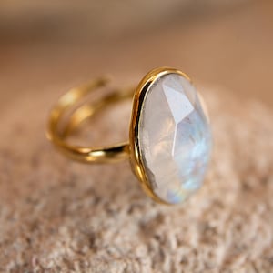 Puede incluir: Un anillo de oro con una gran piedra de luna ovalada. La piedra es clara con un ligero brillo iridiscente.