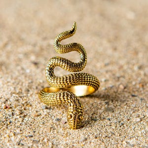 Puede incluir: Un anillo de serpiente de color dorado con una superficie texturizada. La serpiente está enroscada en forma de espiral.