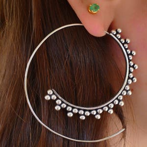May include: Silver hoop earrings with a decorative beaded design. The earrings are large and have a circular shape.