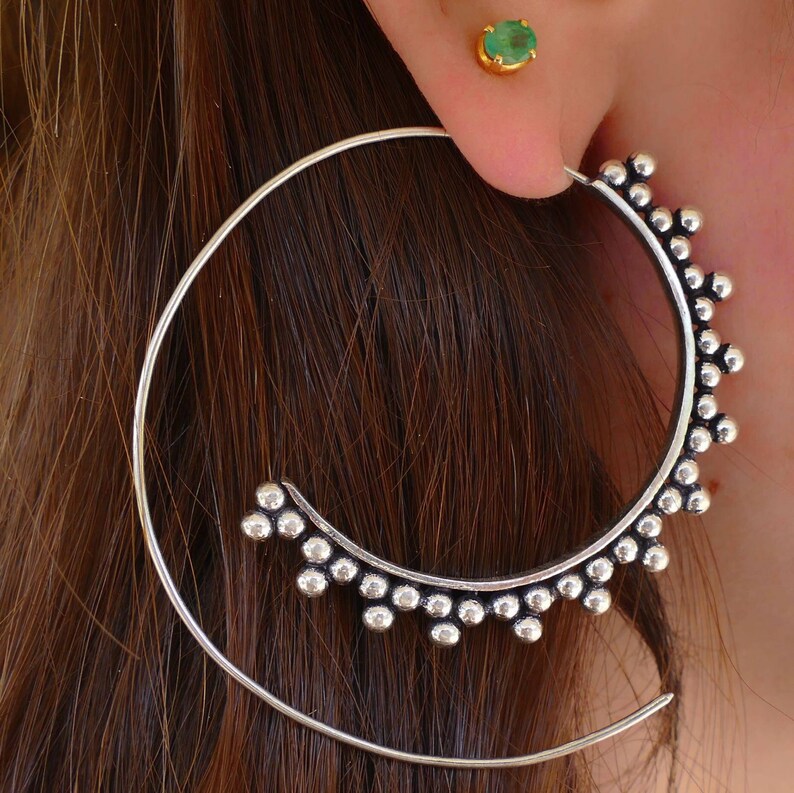 May include: Silver hoop earrings with a decorative beaded design. The earrings are large and have a circular shape.