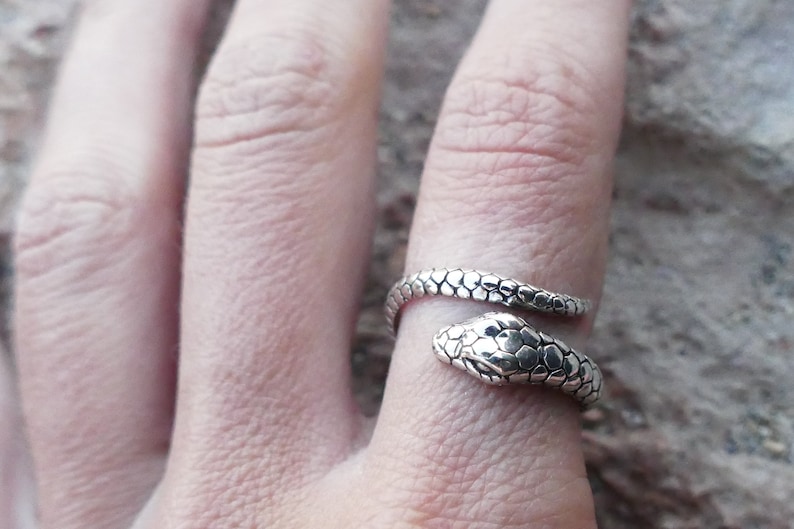 May include: A silver snake ring with a textured finish. The ring is wrapped around a finger.