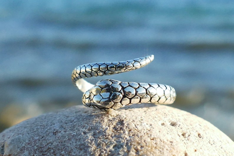 May include: A silver snake ring with a textured, scaly design. The ring is coiled and the snake's head is facing forward.