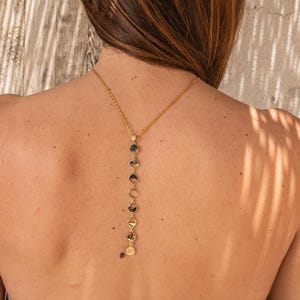May include: A gold chain necklace with a series of round, flat, gold charms hanging from it. The necklace is worn on the back of a person's neck.