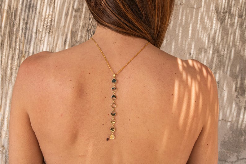 May include: A gold chain necklace with a series of round, flat, gold charms hanging from it. The necklace is worn on the back of a person's neck.