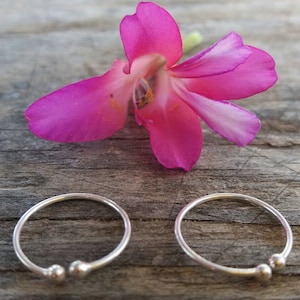 May include: Two silver toe rings with small round beads on a wooden surface. The rings are simple and delicate.