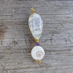 May include: A handcrafted pendant featuring a teardrop-shaped, clear crystal, wire-wrapped in gold-colored metal. Below, a small purple bead and a white, circular shell with a spiral design are attached. The pendant is approximately 3 inches long.