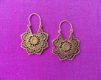 May include: A pair of gold-toned earrings with a delicate mandala design. The earrings are made of metal and have a hoop style.