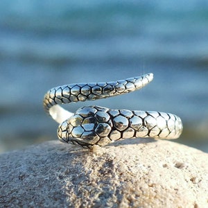 Può includere: Un anello a forma di serpente in argento con un design testurizzato e squamoso. L'anello è avvolto e la testa del serpente è rivolta in avanti.