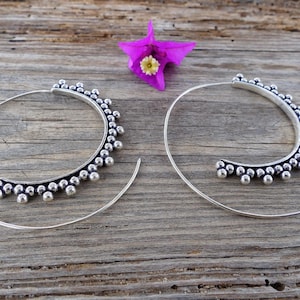 May include: A pair of silver hoop earrings with a beaded design. The earrings are large and have a circular shape.
