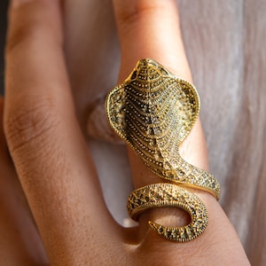 Pode incluir: Um anel dourado em forma de cobra com uma superfície texturizada.