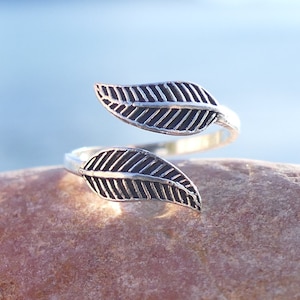 Puede incluir: Un anillo de plata con dos diseños de hojas. El anillo es ajustable y se puede usar en cualquier dedo.