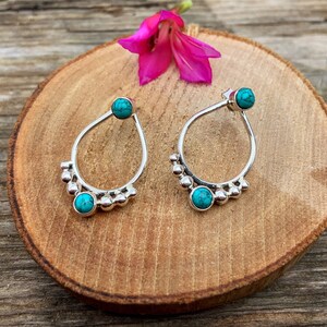 Puede incluir: Un par de pendientes de aro de plata con piedras turquesa. Los aros están decorados con pequeñas cuentas de plata.