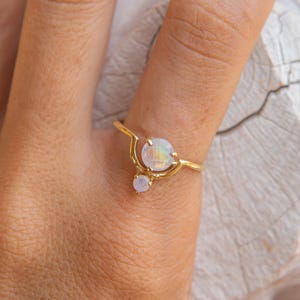 Könnte beinhalten: Ein goldener Ring mit zwei weißen Opal-Steinen. Der Ring hat ein Halbmond-Design.