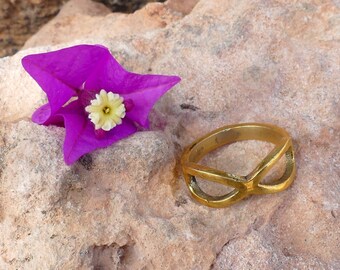 May include: A gold ring with a unique infinity symbol design, resting on a rock next to a vibrant purple flower with a yellow center.