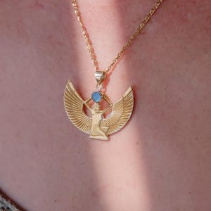 May include: Gold-colored pendant necklace featuring an Egyptian goddess design with outstretched wings and a blue gemstone. The pendant hangs from a delicate chain, creating an elegant accessory.