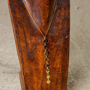 May include: A gold necklace with a chain and multiple round pendant charms. The necklace is displayed on a wooden mannequin.