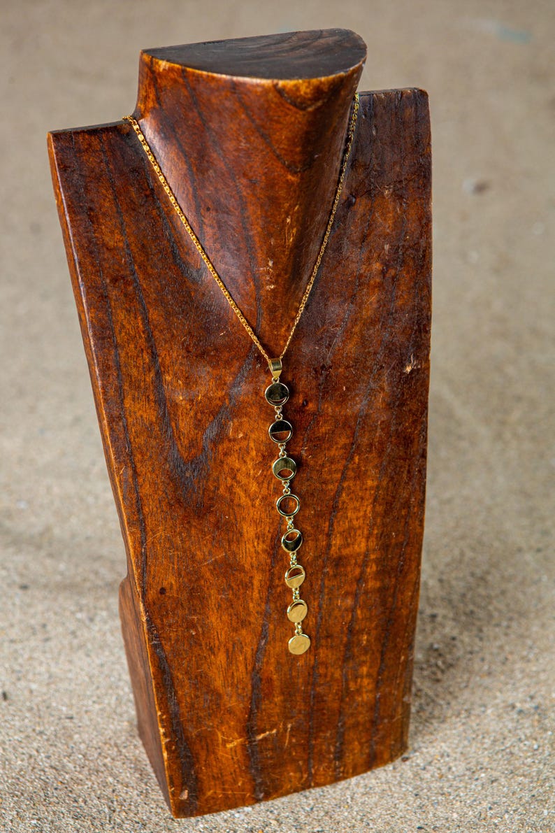 May include: A gold necklace with a chain and multiple round pendant charms. The necklace is displayed on a wooden mannequin.