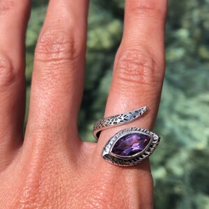 May include: A silver snake ring with an amethyst gemstone. The ring is designed to wrap around the finger.