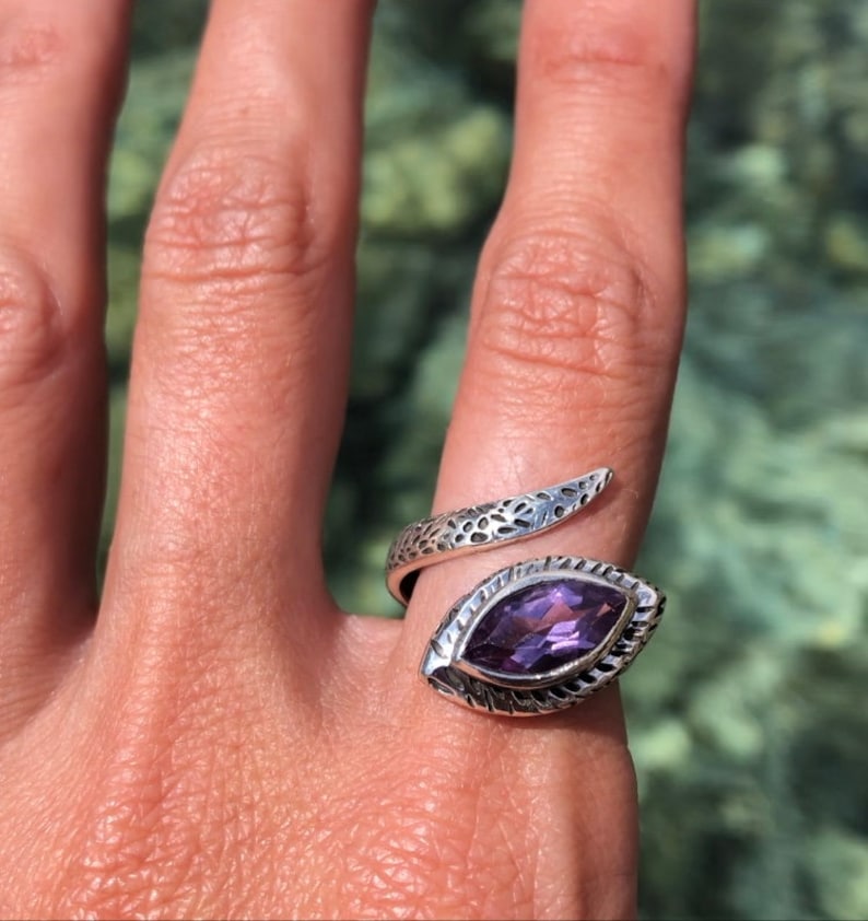 May include: A silver snake ring with an amethyst gemstone. The ring is designed to wrap around the finger.