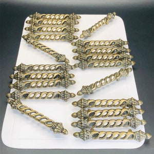 May include: A collection of antique bronze-colored cabinet pulls with a twisted rope design. Each pull has decorative finials on each end. The pulls are arranged on a white surface against a black background.