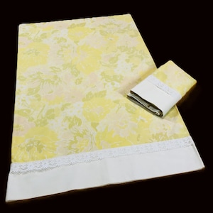 May include: A yellow floral patterned sheet set with a matching pillowcase. The sheets have a white border with lace trim. The floral pattern includes yellow, white, and light green colors. The set is displayed on a dark background.