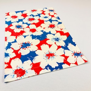 May include: A rectangular fabric piece featuring a bold floral pattern with large white flowers, bright red centers, and deep blue accents. The design consists of repeating stylized blossoms across the entire surface of the textile material.