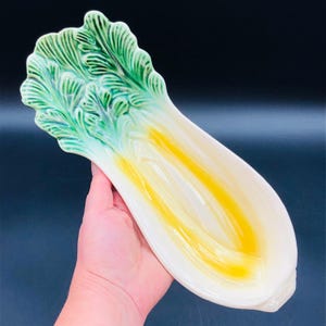 May include: A ceramic serving dish shaped like a head of lettuce. The dish is white with green leaves and a yellow center.