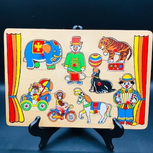 May include: Wooden circus-themed puzzle featuring colorful illustrations of a blue elephant, a clown, a tiger, a seal balancing a ball, a monkey on a bicycle, a horse, a clown playing an accordion, and a car with a clown.