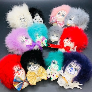 Peut inclure: Une collection de poupées clowns avec des cheveux en fourrure duveteuse de différentes couleurs, dont le rouge, le bleu, le rose et le violet. Chaque poupée a un visage peint avec un nœud papillon ou un ruban. Les poupées sont disposées sur une surface sombre.