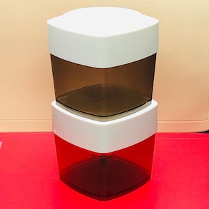 May include: Two-piece, stackable storage containers. The top section is white, and the bottom section is transparent brown. The lower container is red with a white top. The containers are square with a slightly angled design.