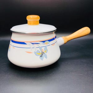 May include: White enamel saucepan with a wooden handle and lid. The pot features a blue and peach floral design with a silver rim. The handle and lid knob are made of light-colored wood.