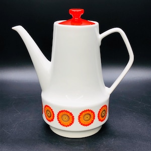 Puede incluir: Cafetera de cerámica blanca con tapa roja y una banda de flores naranja y marrón alrededor de la base.