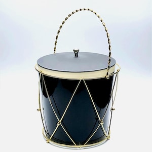May include: A black ice bucket with a gold-colored metal frame and handle. The bucket has a lid and a decorative diamond pattern on the sides. The handle is twisted and adds a touch of elegance.