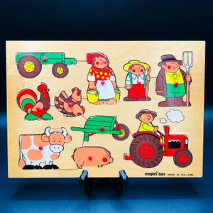 May include: Wooden farm puzzle with a tractor, farmer, and farm animals. The colourful puzzle pieces include a rooster, cow, pig, and wheelbarrow. The puzzle is designed for young children. The puzzle is made in Holland.