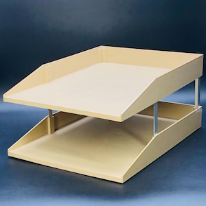 May include: A two-tiered beige plastic desk organizer with a slanted top shelf. The organizer is made of a sturdy plastic and has a modern design.