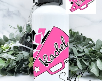 Könnte beinhalten: Eine weiße Wasserflasche mit einem rosafarbenen Megaphon-Design und dem Namen "Rachel" in Schwarz. Das Megaphon hat einen schwarzen Stern und die Worte "Cheerleader" sind in Schwarz geschrieben. Die Worte "Sugar + Faith" sind in Schwarz am Boden der Flasche geschrieben.