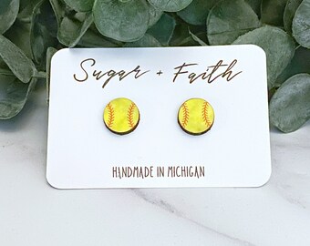 Peut inclure: Une paire de boucles d'oreilles en bois avec un motif de balle de softball. Les boucles d'oreilles sont jaunes avec des coutures rouges et sont faites à la main au Michigan. La carte indique "Sugar + Faith".