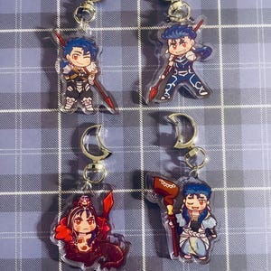 May include: Four colourful anime character keychains with silver key rings. The characters are drawn in a chibi style and are holding weapons. The keychains are made of clear acrylic.